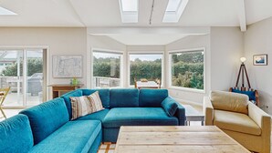 Ein modernes Wohnzimmer mit einem Ecksofa, einem Couchtisch aus Holz und großen Fenstern mit Blick auf Grünflächen.