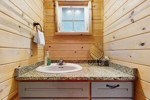 A wooden cabin bathroom with a granite countertop, a white sink, a window, and a towel rack. - Cozy family friendly cottage near ocean with loft, washer&dryer and WIFI (Manzanita)