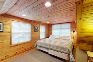 A wooden cabin bedroom with a bed, two windows, a ceiling light, and a small table. - Cozy family friendly cottage near ocean with loft, washer&dryer and WIFI (Manzanita)
