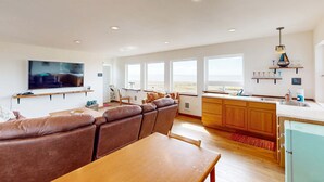 Ein modernes Wohnzimmer mit einer Couch, einem Esstisch, einem Fernseher und einer Küchenzeile mit Holzschränken und einem Spülbecken.