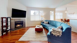 Un salon avec une cheminée, un canapé bleu, une table basse et un téléviseur à écran plat fixé au mur.