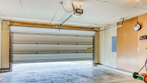 Un garage avec une porte à enroulement fermée, un luminaire fixé au plafond, un panneau perforé mural et une tondeuse à gazon verte.
