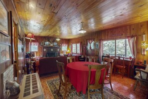Interior de una cabaña de madera con comedor, chimenea y ventanas amplias.