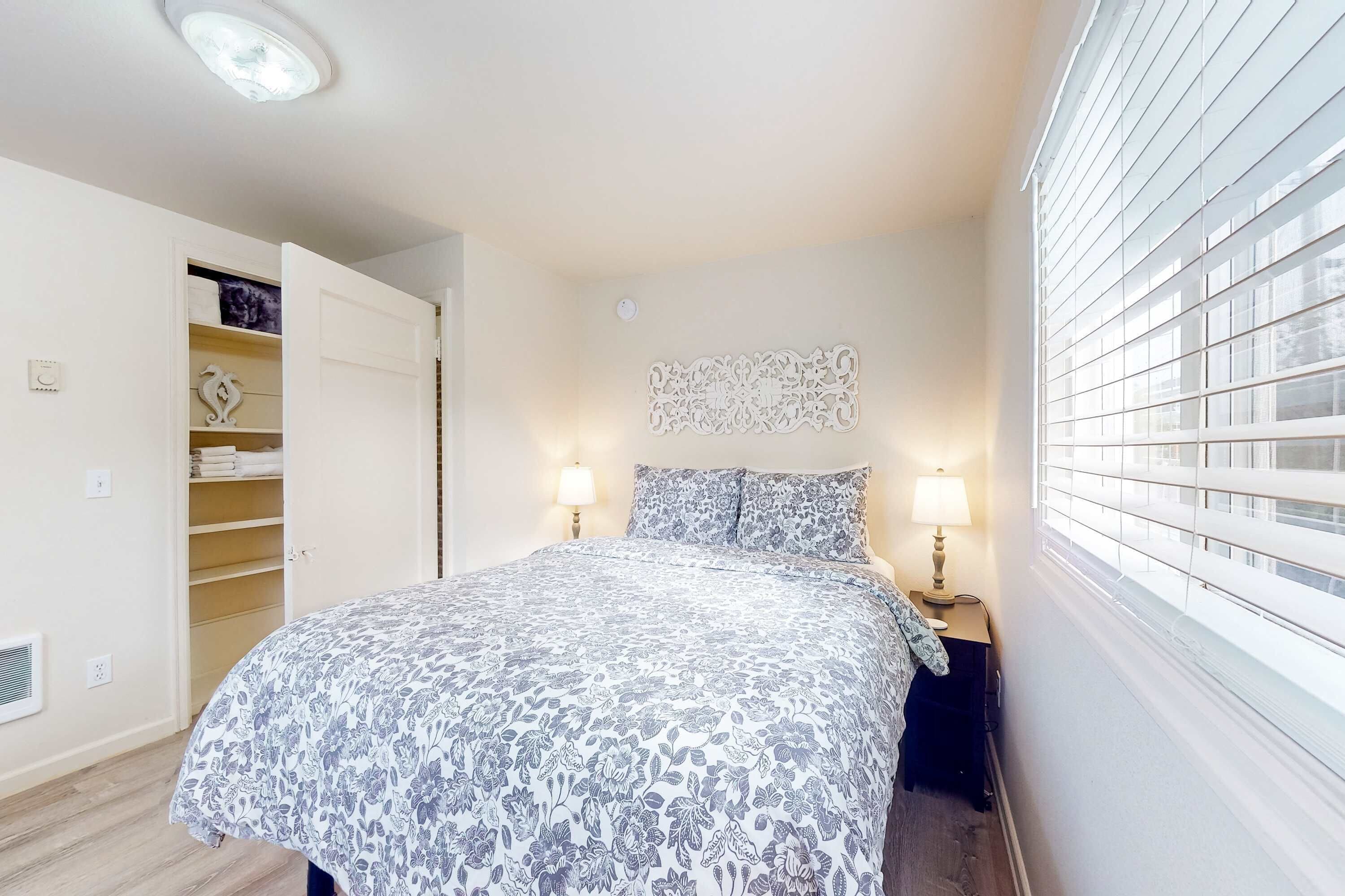 A bedroom with a bed, bedside lamps, a wardrobe, and a window with blinds.