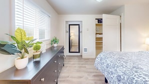 A bedroom with a bed, dresser, potted plants, and a mirror.