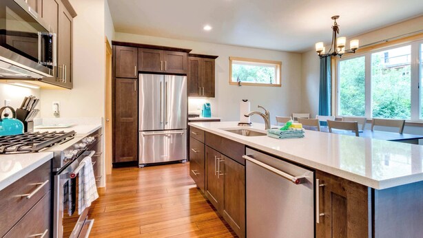 A modern kitchen with stainless steel appliances, wooden cabinets, a large island, and a view of greenery outside. - Kid-friendly house with fireplace, entertainment, and nearby beach access (Manzanita)