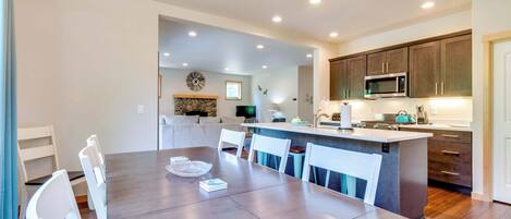 A modern kitchen with dark cabinets, a microwave, and a dining area with a wooden table and white chairs.