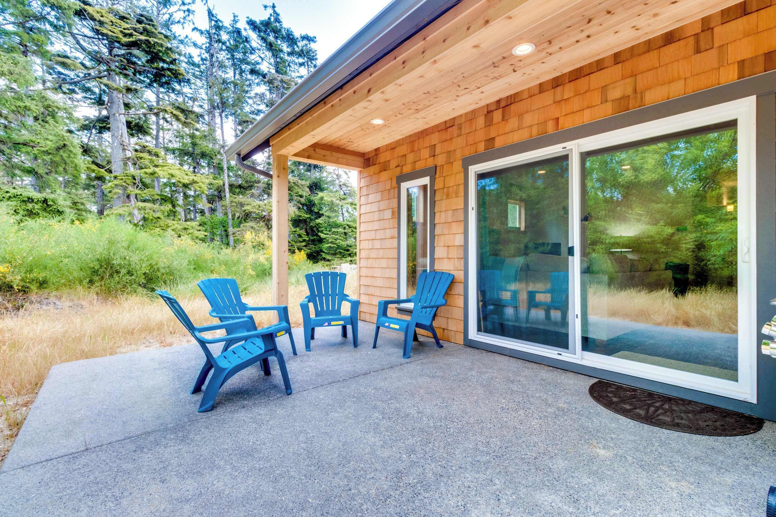 Une façade en bois avec un patio couvert comprenant quatre chaises Adirondack bleues.