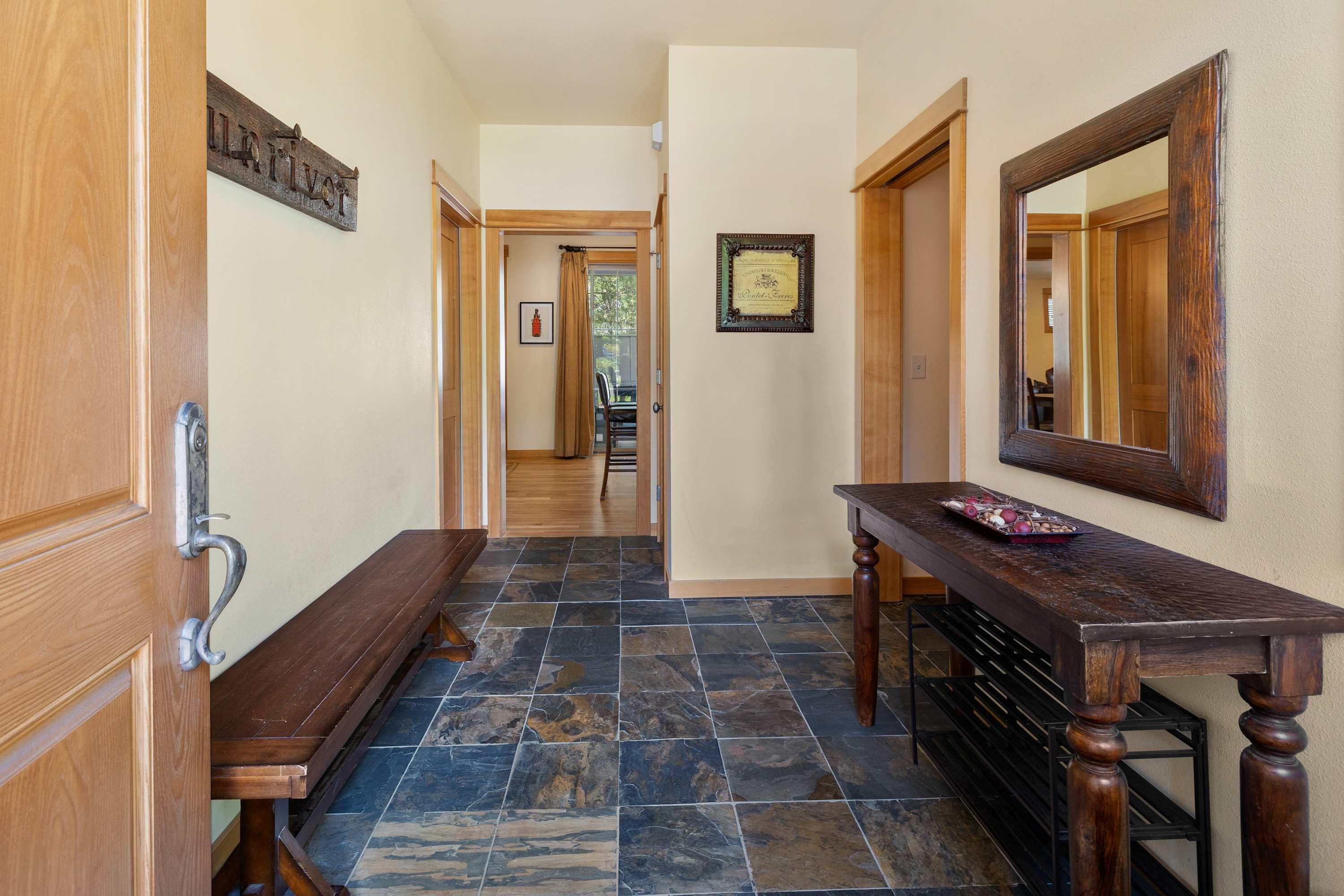 A hallway with a wooden bench, a dark wooden table, and a mirror on the wall.