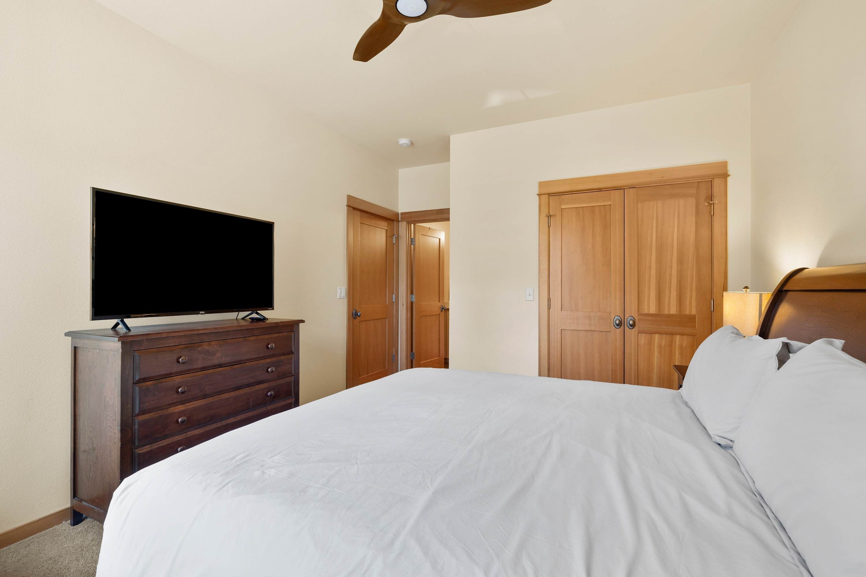 A bedroom with a bed, a dresser, a television, and wooden doors.