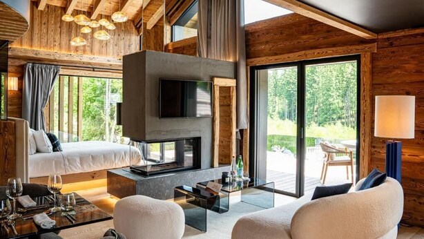 Un interior moderno con chimenea, sofá y zona de comedor, con vigas de madera y ventanas amplias.