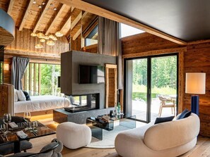 Ein modernes Interieur mit Kamin, einer Couch und einem Essbereich, mit Holzbalken und großen Fenstern.