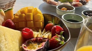 Una mesa con diversas frutas y un vaso de jugo, con montañas al fondo.
