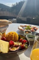 A table with a variety of fruits and a glass of juice, set against a mountainous backdrop.