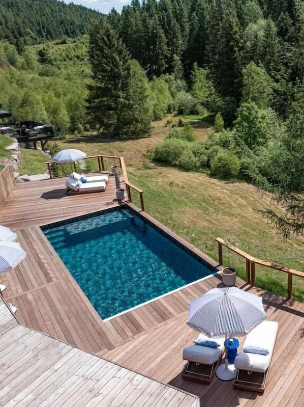 Ein rechteckiger Pool mit Holzterrasse, umgeben von Liegestühlen und Sonnenschirmen.