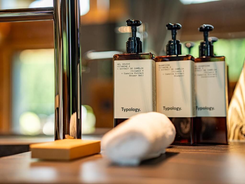 Trois bouteilles de gel douche de la marque Typology, posées sur une surface en bois, avec une serviette blanche à proximité.