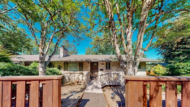 A two-story stone house with a front porch, a wooden deck, and a clear sky. - Upper level of duplex with a large deck & mountain view - dog friendly for 1 dog (Eugene)