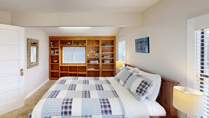 Ein Schlafzimmer mit einem Bett, einem hölzernen Bücherregal, einem Fenster mit Jalousien und einem gerahmten Bild an der Wand.