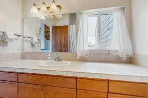 Un baño con lavamanos, espejo, armarios de madera y una ventana con cortinas.