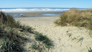 Ein sandiger Strand mit Dünen und im Hintergrund Meereswellen.