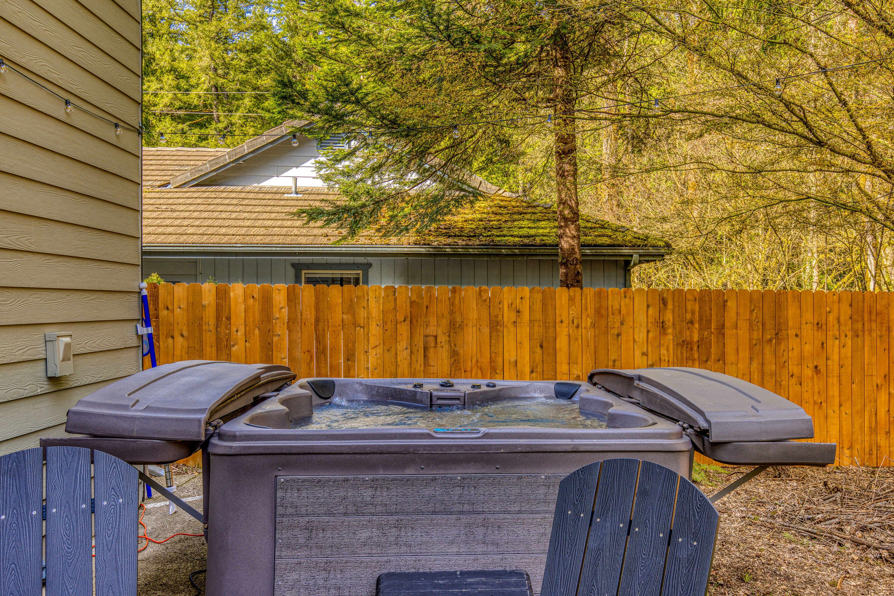 A hot tub with two seats, a wooden fence, and a house in the background.
