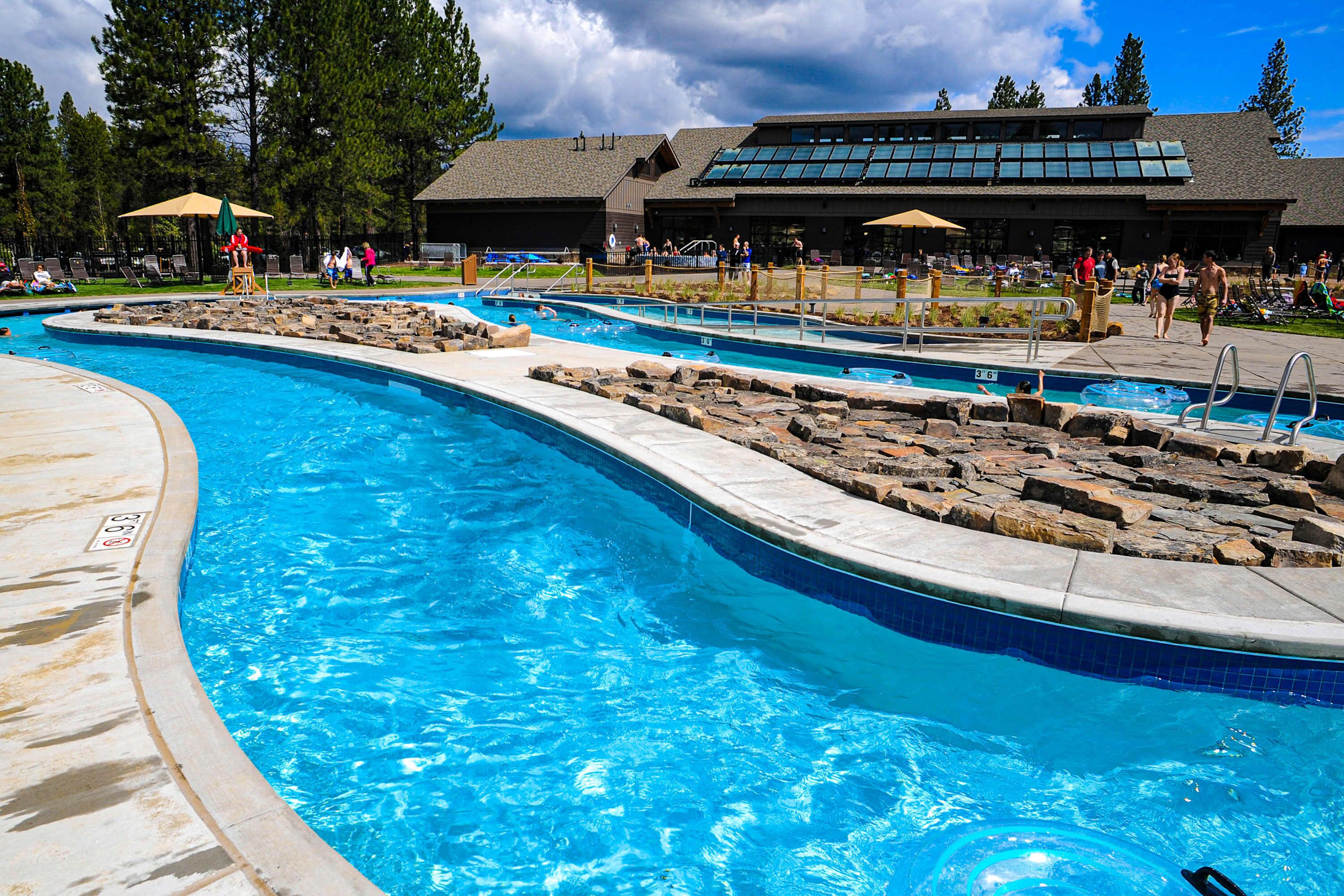 A swimming pool with multiple lanes, a lifeguard chair, and a building with large windows in the background.