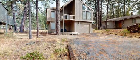 A two-story cabin with a balcony, surrounded by tall pine trees.