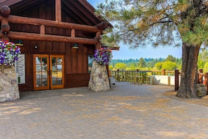 A wooden lodge with stone pillars, a wooden deck, and a view of trees and mountains. - Charming home with fireplace, hot tub, WiFi, SHARC access, bikes (Sunriver)