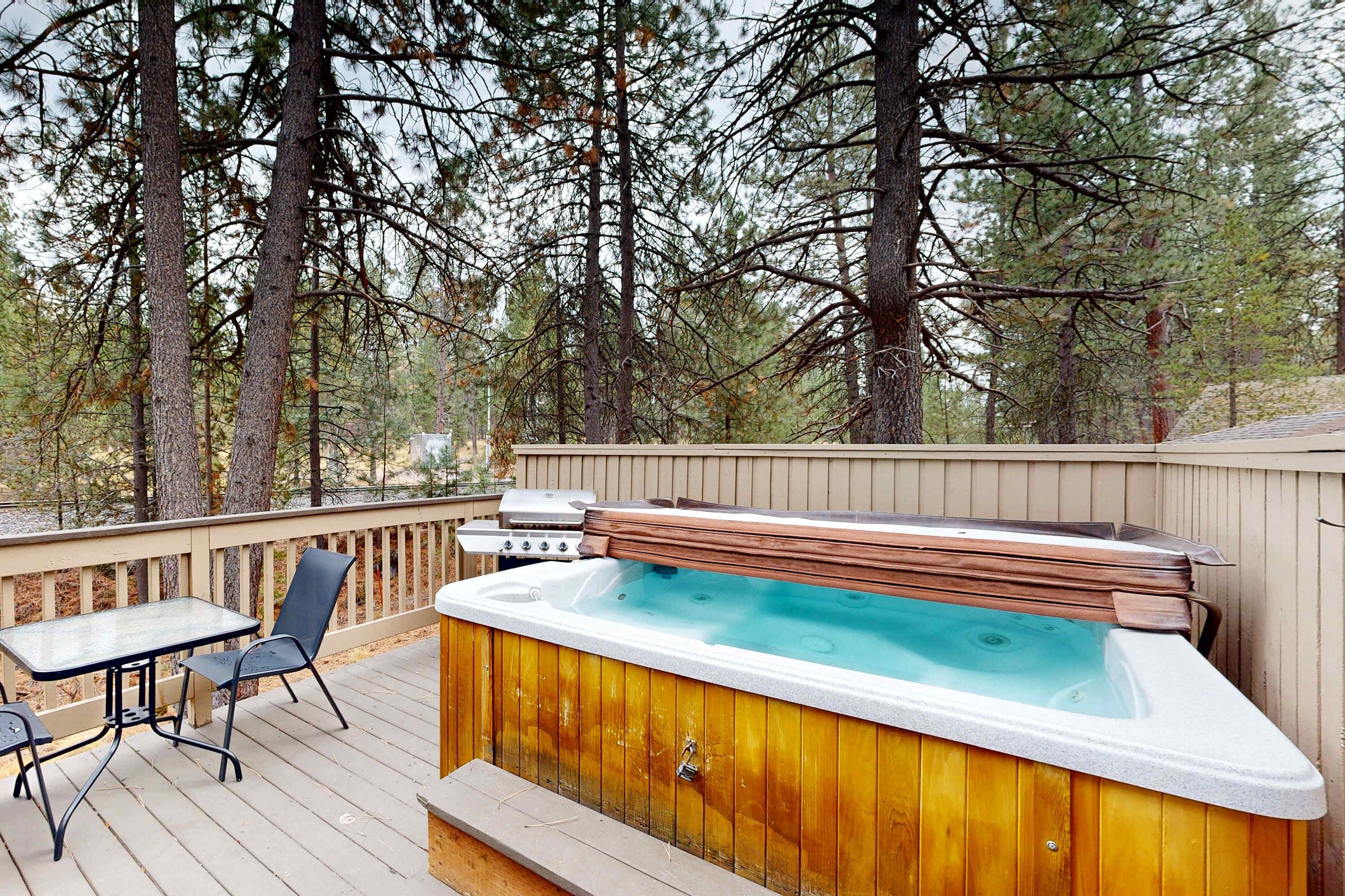 A hot tub on a wooden deck with a table and chairs, surrounded by trees.