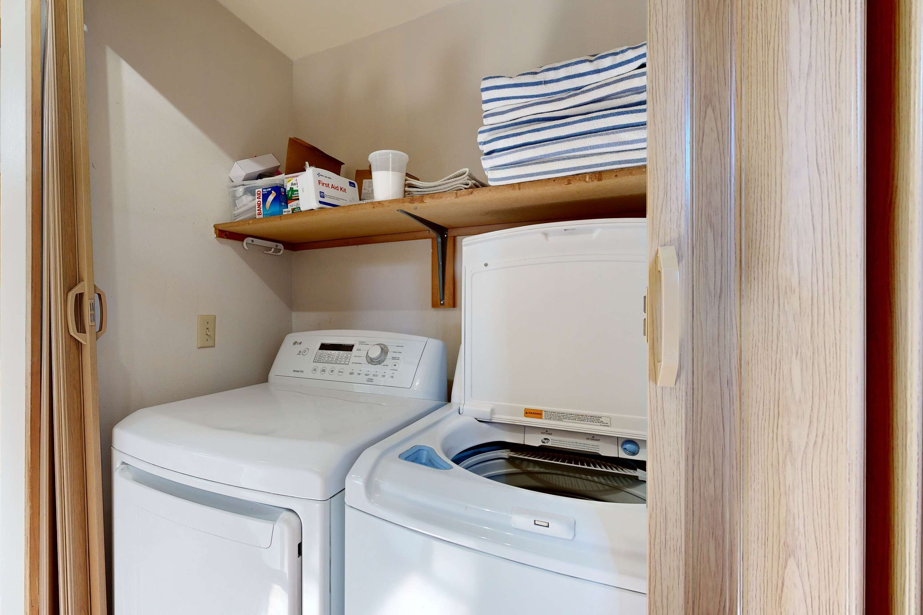 A laundry area with a washing machine, dryer, and a shelf with folded towels and a cup.