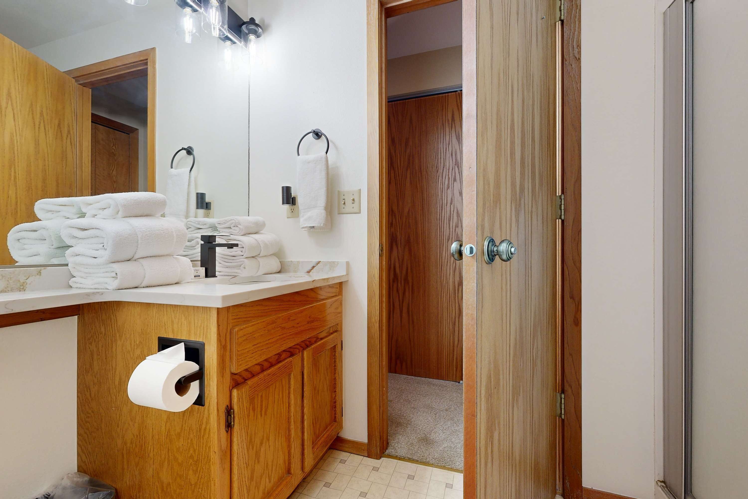 Een badkamer met een houten wastafelmeubel, een spiegel, een handdoekhouder en een toiletrolhouder.