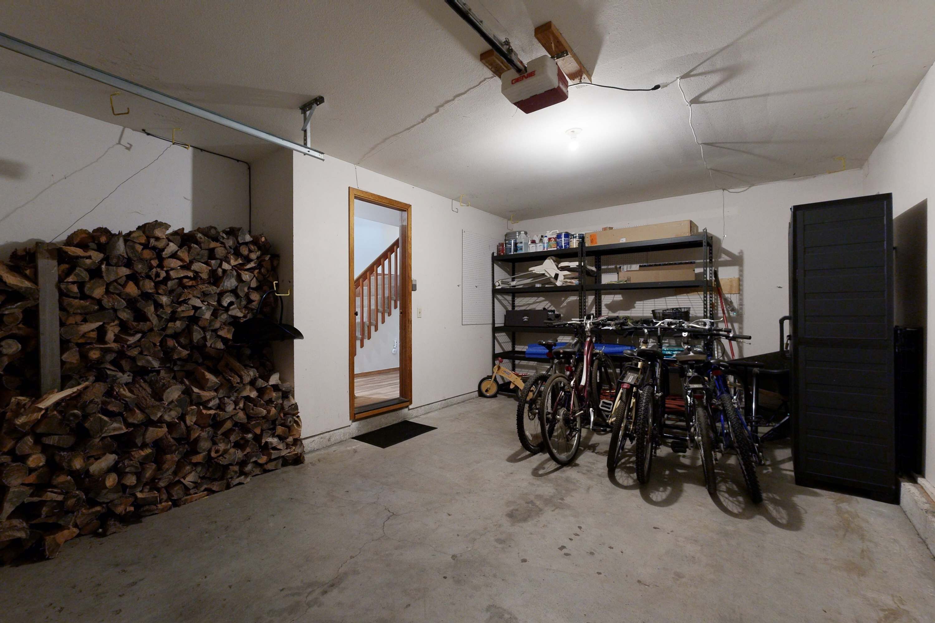 Un garage où sont entreposés du bois de chauffage, des vélos et où est installé un ventilateur de plafond.