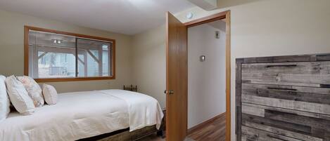 A bedroom with a bed, a window with blinds, a wooden wardrobe, and a ceiling light fixture.