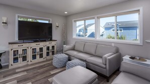 A living room with a sofa, ottoman, TV, and built-in entertainment unit. - Charming dog-friendly home with ocean-view, beach access, & washer/dryer (Bandon)