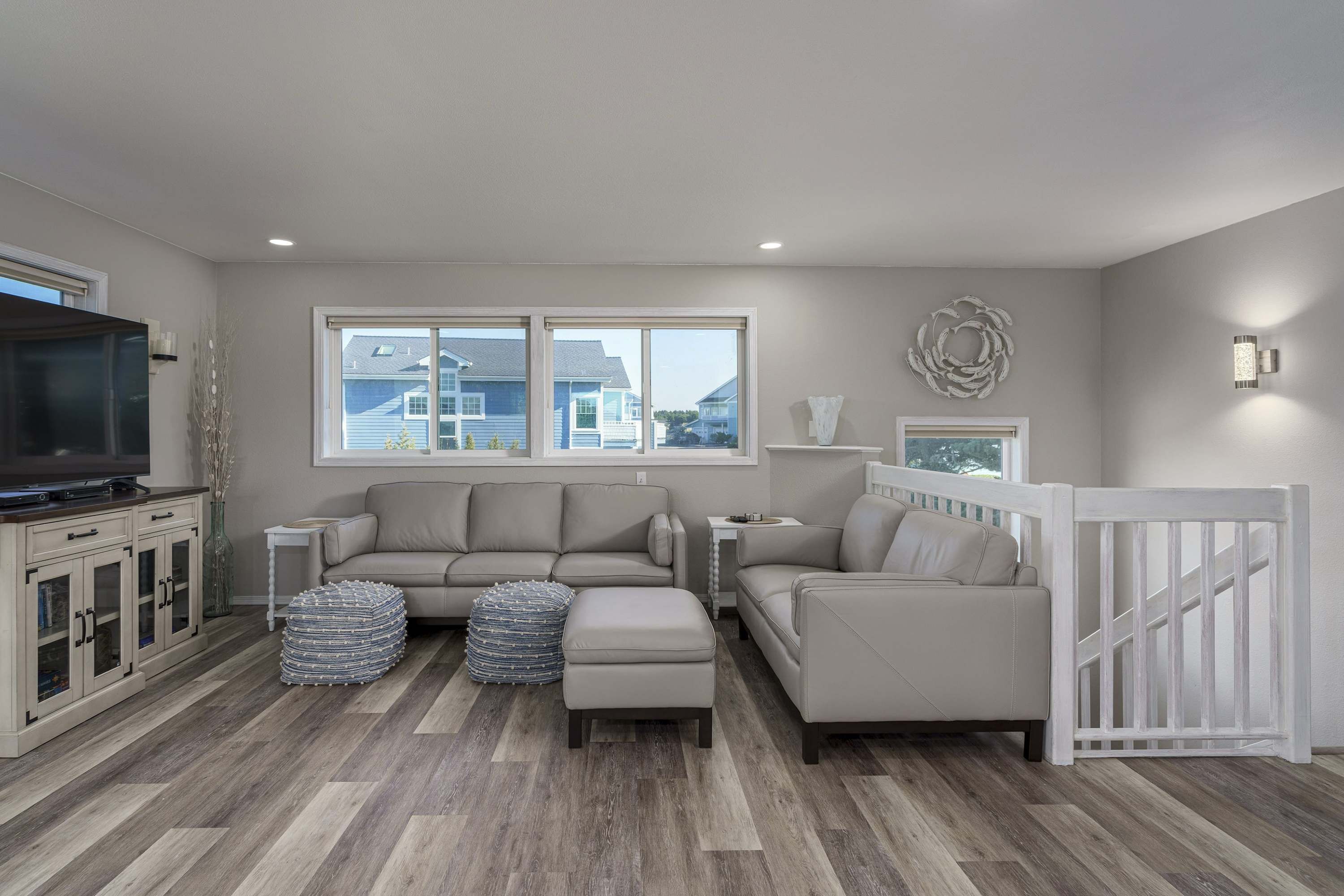 A living room with a sectional sofa, ottoman, TV stand, and a white railing.