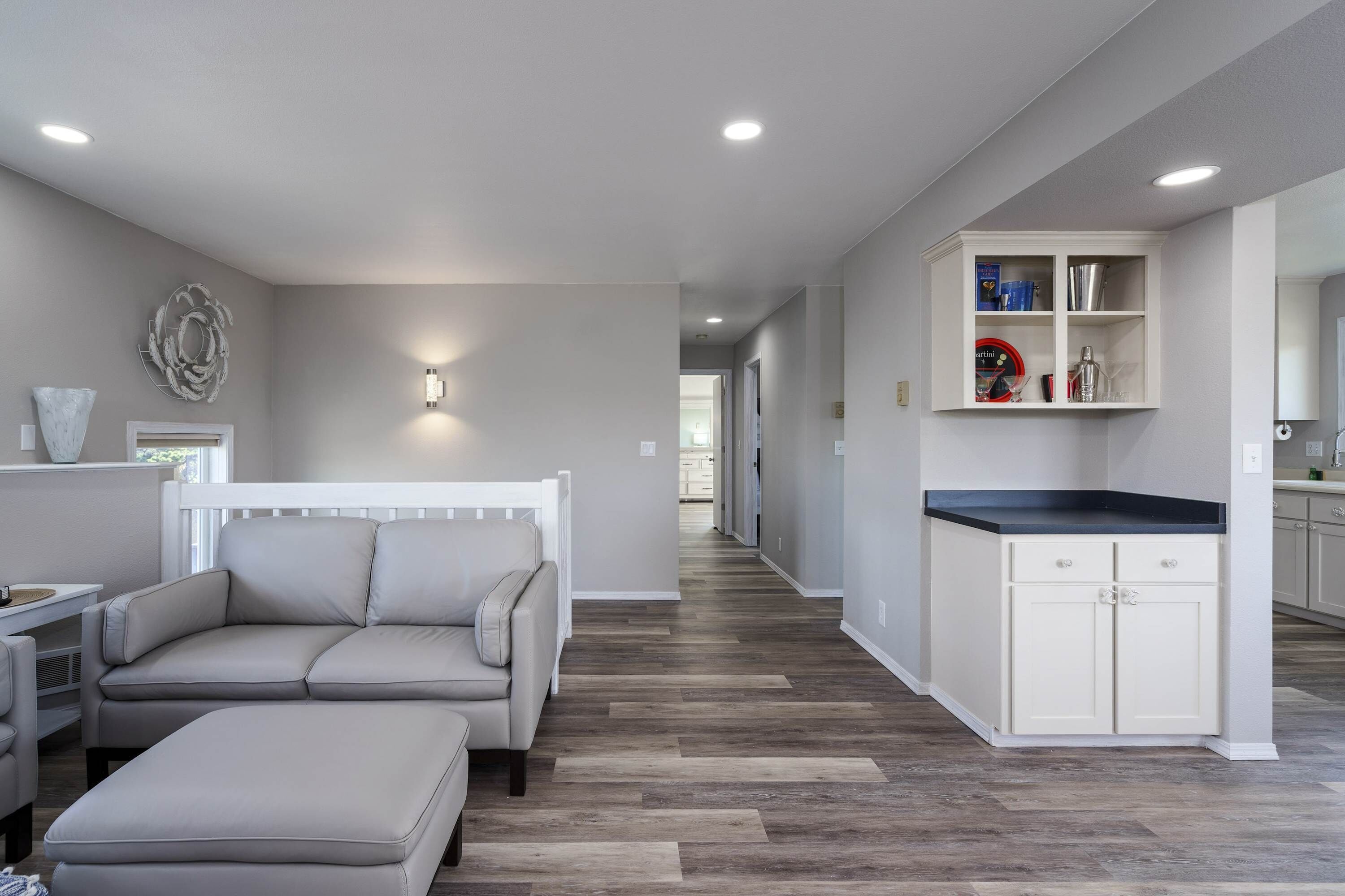Un intérieur moderne comprenant un canapé, un pouf et un coin cuisine avec des placards et un plan de travail.