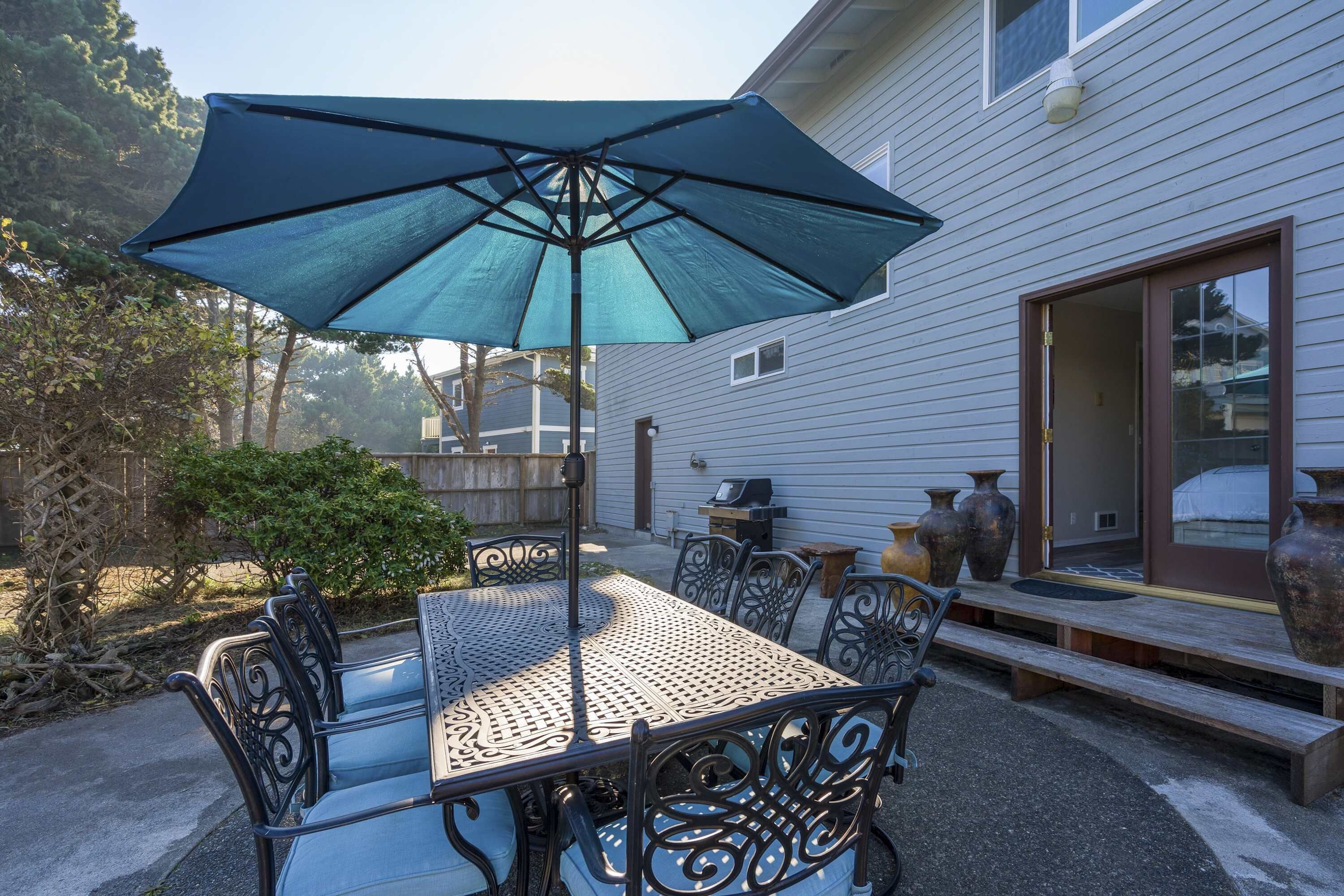 Une terrasse extérieure avec une table et des chaises, un grand parasol, et une maison en arrière-plan.