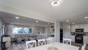 A modern kitchen with white cabinetry, a dining area with a white table and chairs, and a living area with a sofa and ottomans. - Charming dog-friendly home with ocean-view, beach access, & washer/dryer (Bandon)