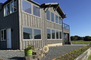 A two-story building with large windows, a balcony, and a gravel driveway.