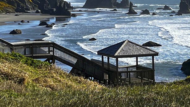 Ein Küstenweg führt zu einem Gazebo mit Blick auf den Ozean, im Hintergrund Felsformationen.