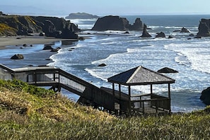 A coastal walkway leading to a gazebo overlooking the ocean with rocky formations in the background.