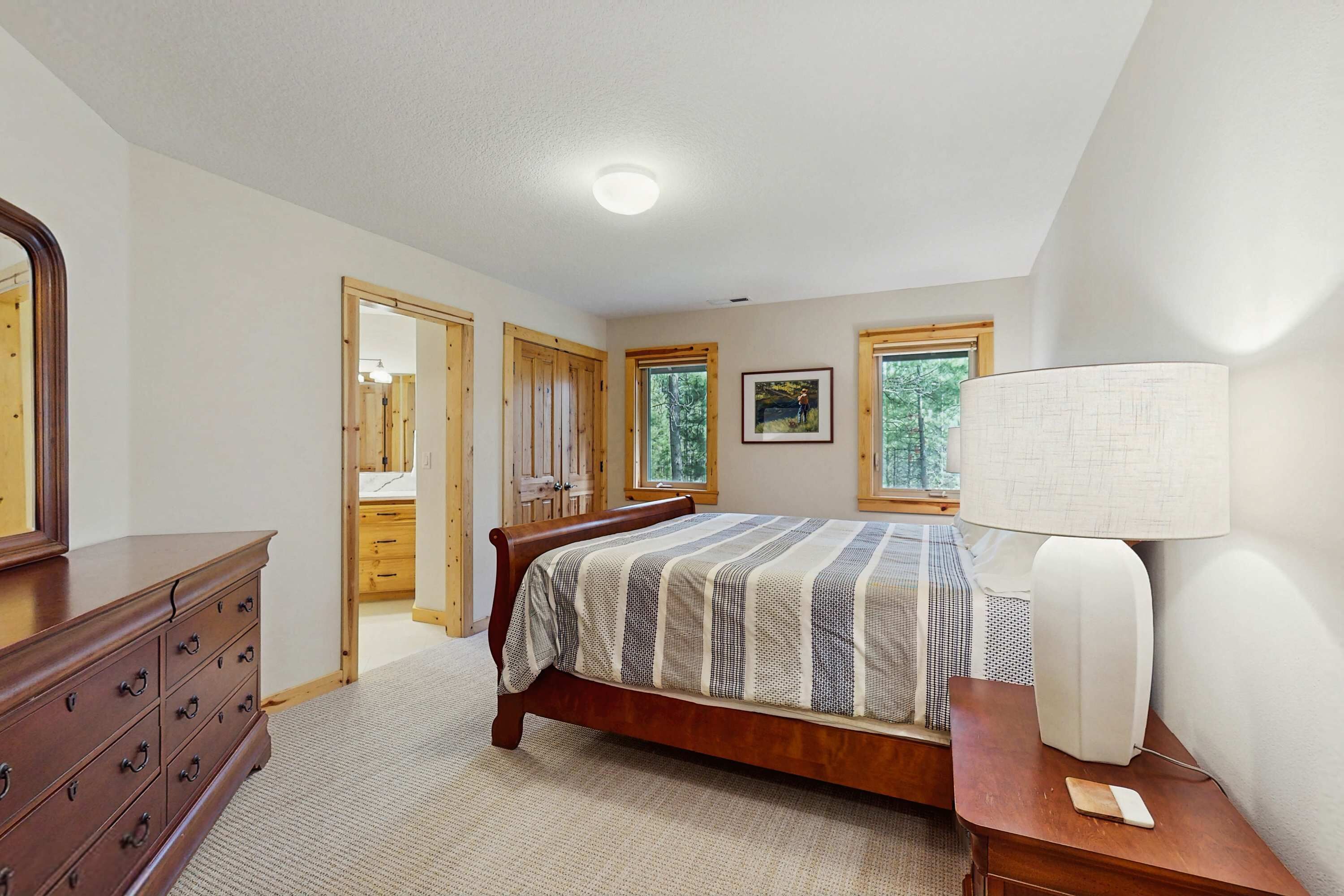 A bedroom with a bed, dresser, lamp, and windows.