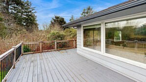 Une terrasse en bois avec une rambarde, de grandes fenêtres et une vue sur les arbres.