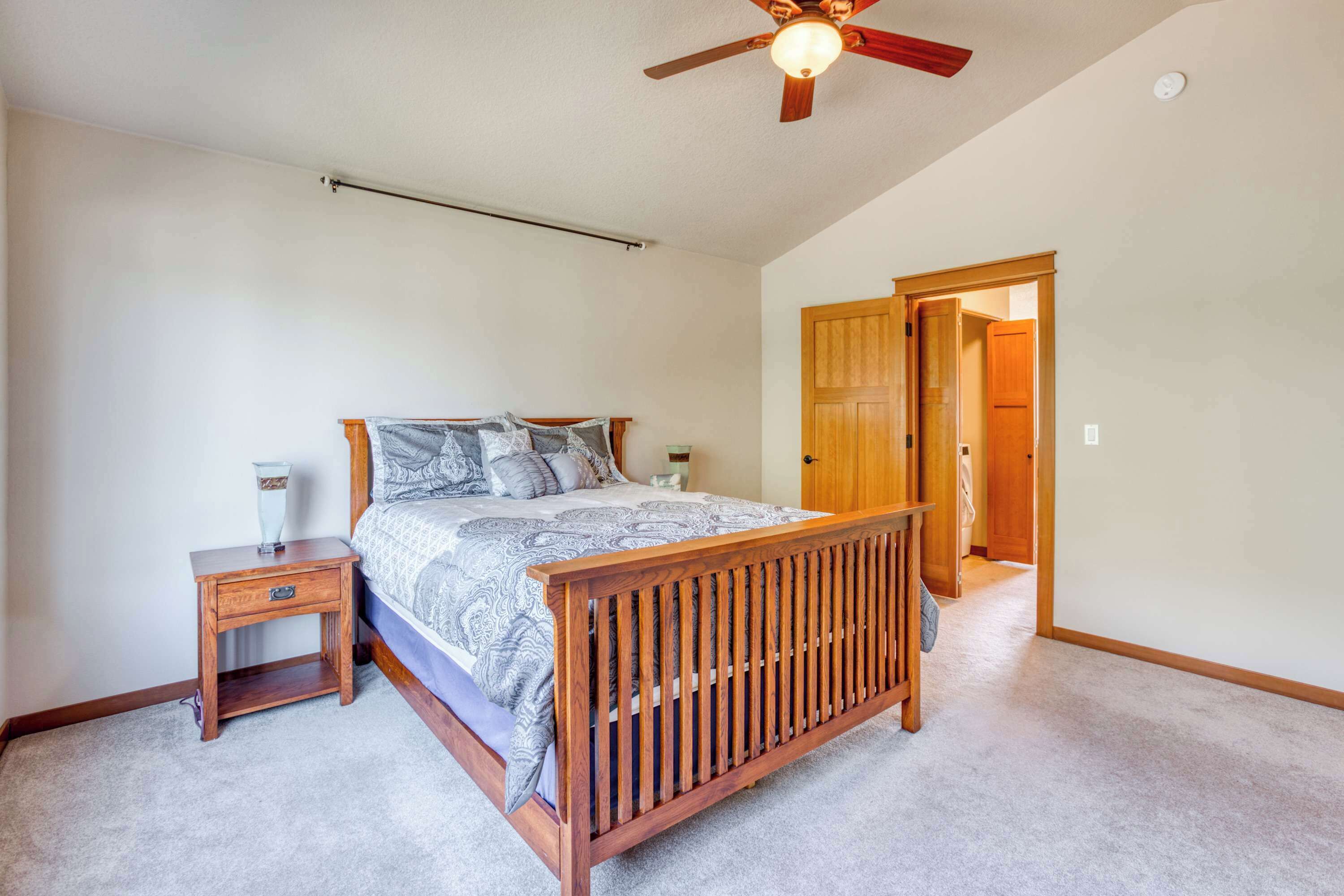 Une chambre à coucher avec un lit en bois, une table de chevet, un ventilateur de plafond et une porte donnant sur une autre pièce.