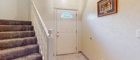 A staircase with a white railing, a white door with a stained glass window, and a framed picture on the wall.