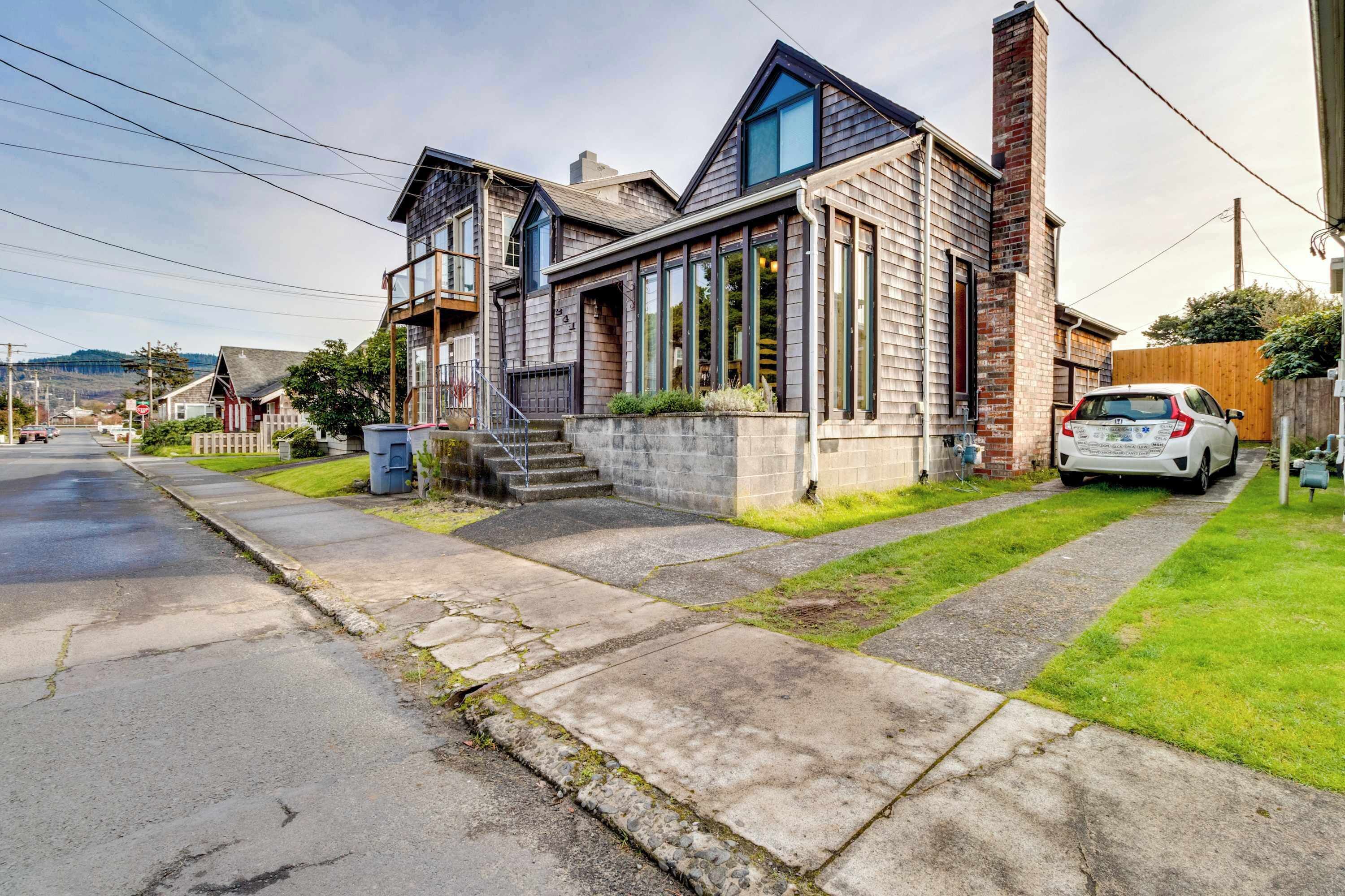 Une maison moderne à deux étages, dotée d’une cheminée imposante, de grandes fenêtres et d’un garage bien visible.