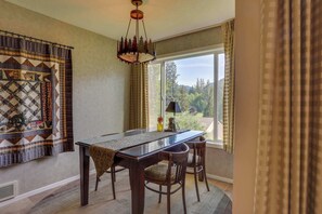 A dining area with a table, chairs, a chandelier, and a view through a large window.
