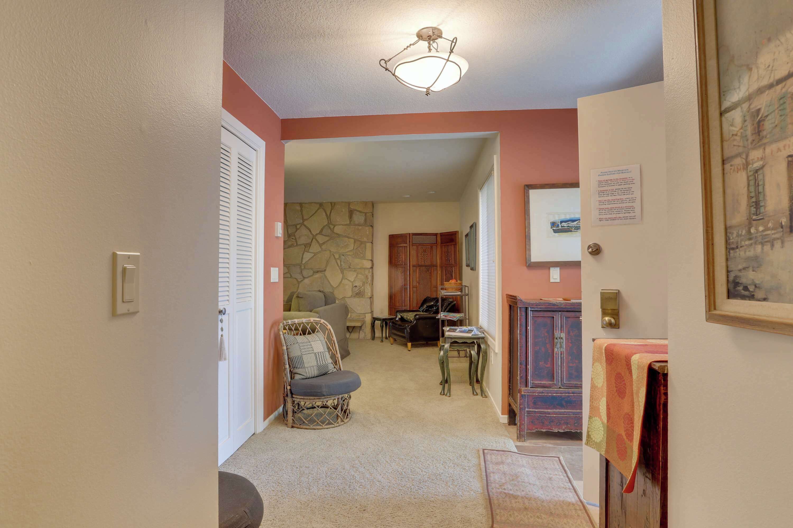 A hallway with a stone wall, a wicker chair, a wooden cabinet, and a framed picture on the wall.