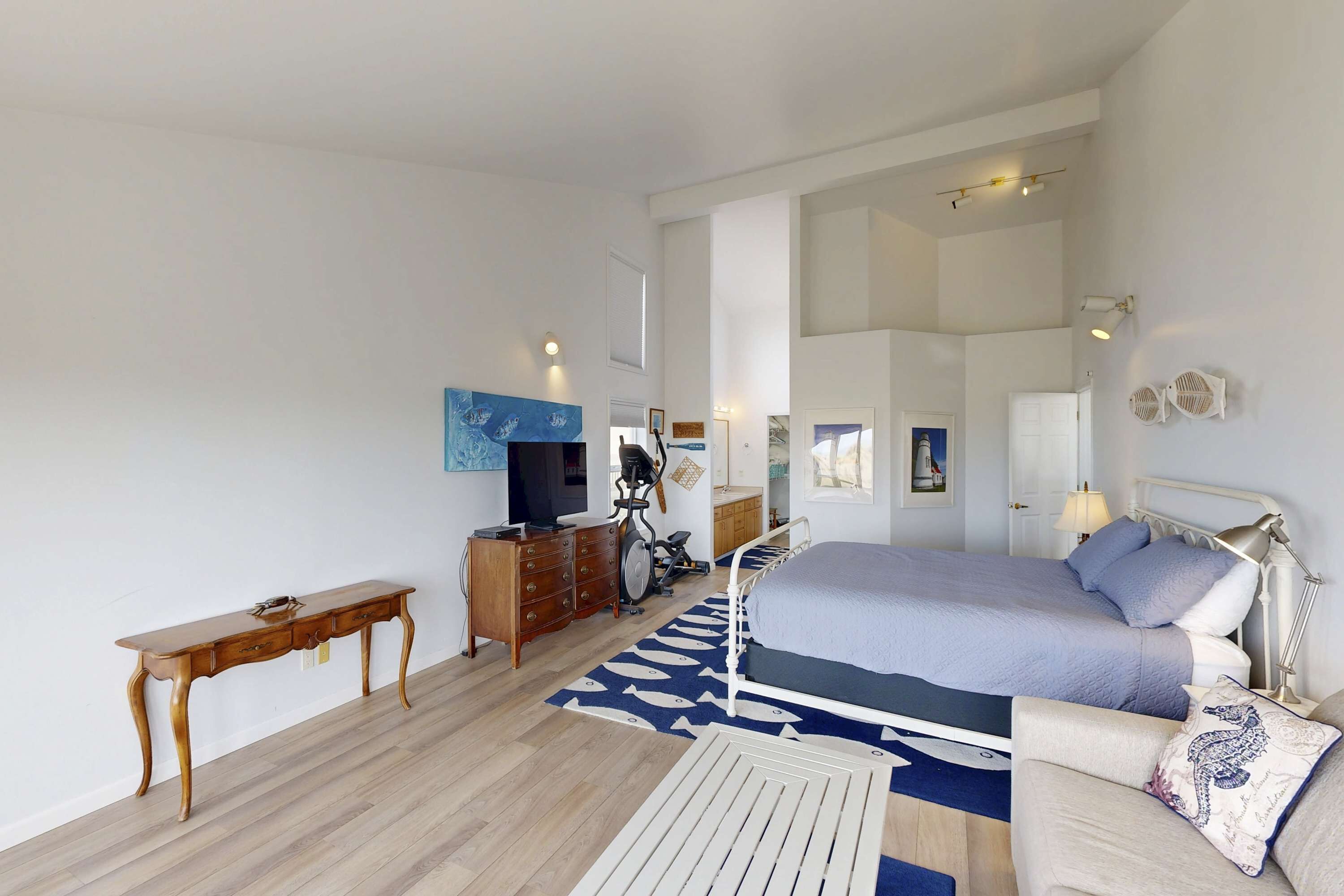 A bedroom with a bed, dresser, exercise bike, and a desk.