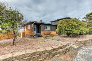 A two-story house with a front porch, a small garden area, and a stone retaining wall.